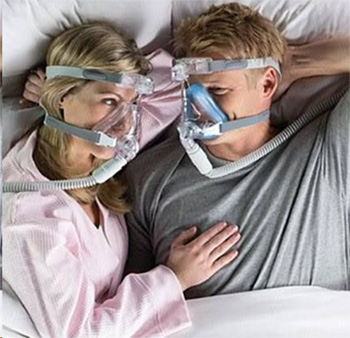 A couple wearing CPAP face masks layomh in bed